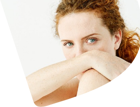 Eine Frau blickt direkt in die Kamera. Sie verdeckt die untere Hälfte ihres Gesichts mit ihrem Arm. 