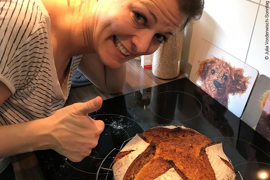 Julia beugt sich über einen Laib Brot und hält den Daumen nach oben. 