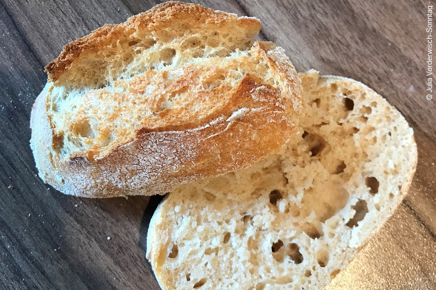 Ein aufgeschnittenes Brötchen auf einem Holztisch. 