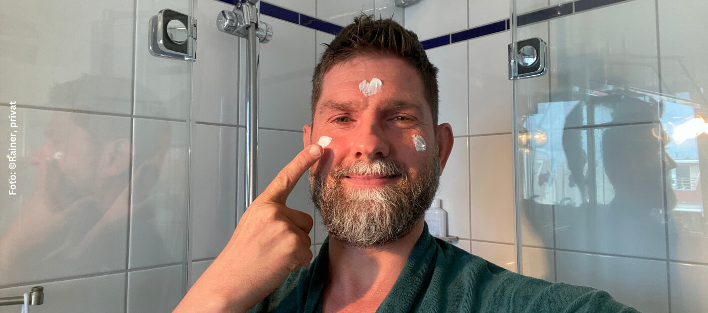 Rainer steht vor dem Spiegel und cremt sein Gesicht ein.