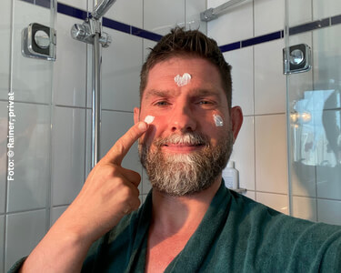 Rainer steht vor dem Spiegel und cremt sein Gesicht ein.