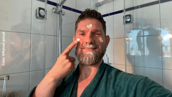 Rainer steht vor dem Spiegel und cremt sein Gesicht ein.