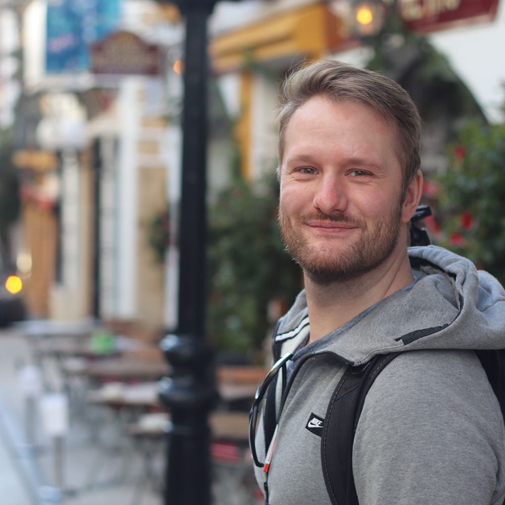 Patrick schaut über die Schulter und lacht in die Kamera.