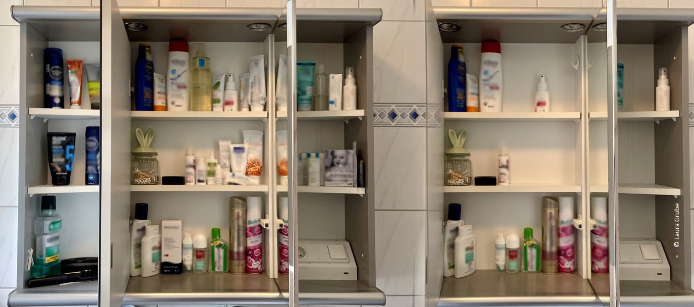 Lauras geöffneter Badezimmerschrank. Darin befinden sich verschiedene Hygiene- und Pflegeprodukte.