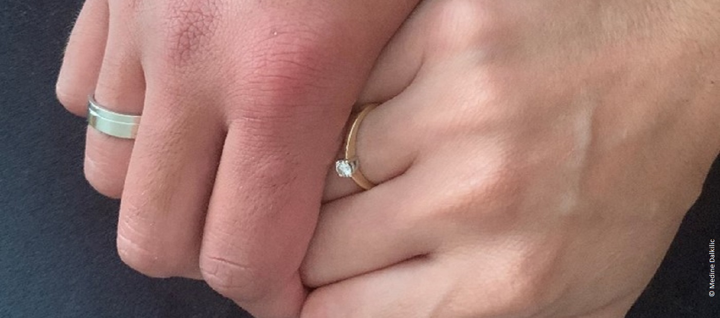 Die Hände von Medine und ihrem Mann. Beide halten sich gegenseitig und tragen einen Ehering. 