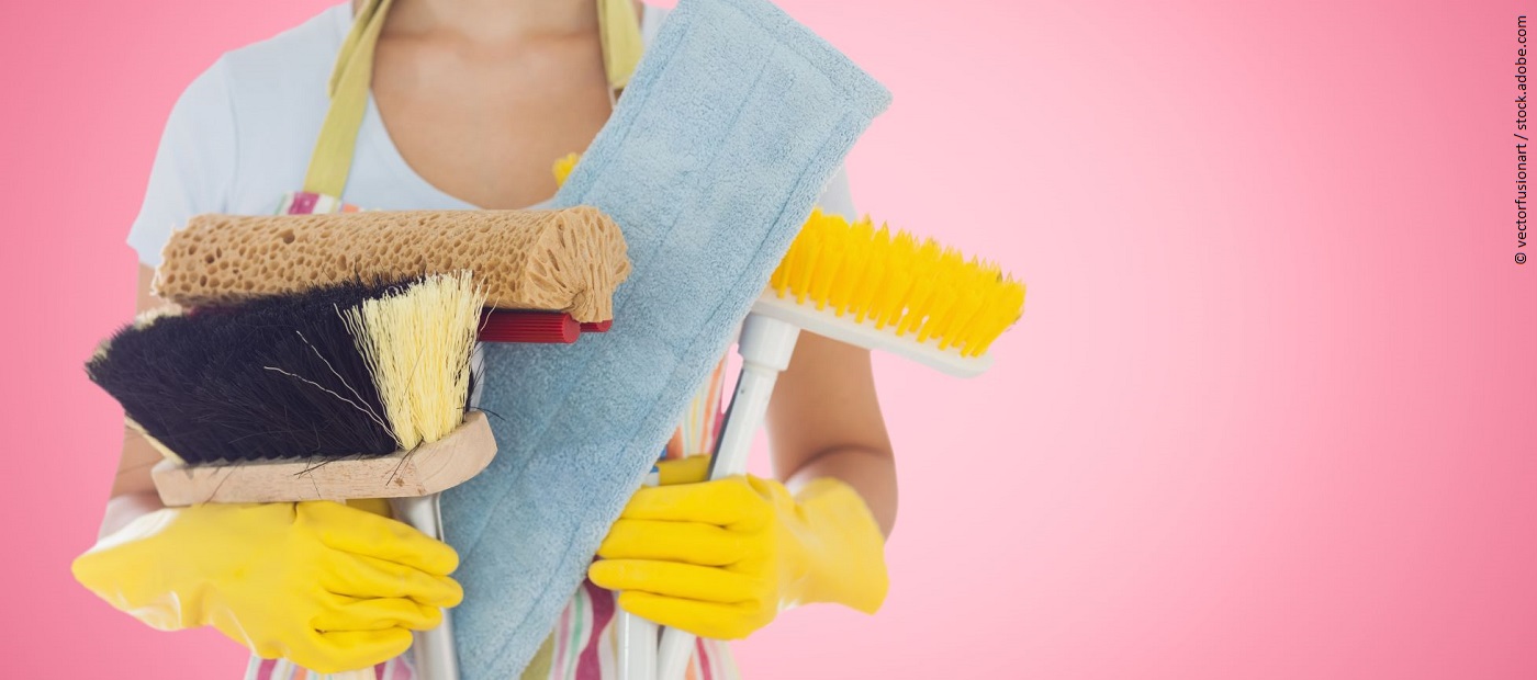 Eine Frau ist vom Hals abwärts zu sehen. Sie trägt Putzhandschuhe und verschiedene Putzmaterialien. 