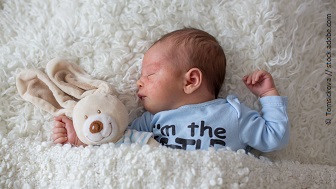 Ein Baby liegt unter zusammen mit einem Plüschhasen unter einer Decke und schläft.