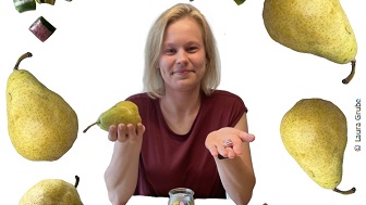 Laura sitzt ein einem Tisch und hält eine Birne in der Hand.  