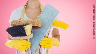 Eine Frau mit gelben Putzhandschuhen hält verschiedene Reinigungsutensilien in der Hand.