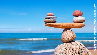 Eine Steinbalance Figur. Im Hintergrund ist ein Strand zu erkennen. 