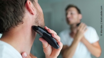 Ein Mann steht vor dem Spiegel und rasiert sich mit einem Elektrorasierer.
