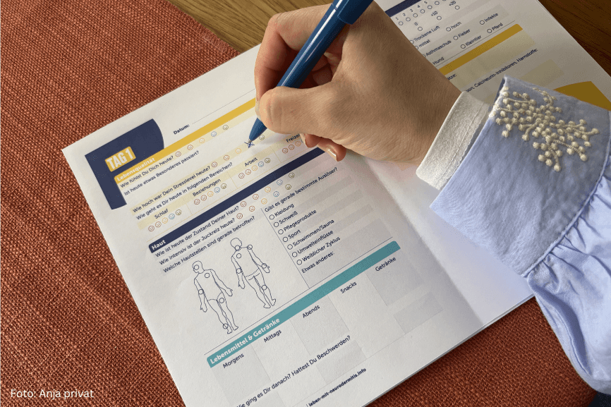 Hand mit Stift füllt ein Ernährungs- und Symptomtagebuch bei Neurodermitis aus