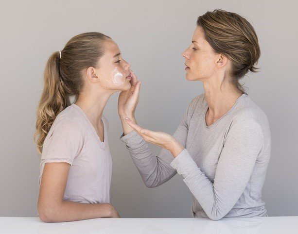 Eine Mutter trägt Creme auf die Wange ihrer Tochter auf.