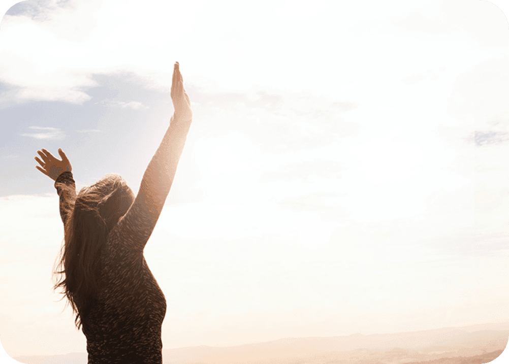 Frau blickt in den Himmel und streckt die Arme in die Luft