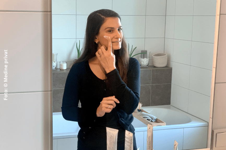Medine cremt sich ihr Gesicht vor dem Badspiegel ein, um Ihre Neurodermitis zu pflegen