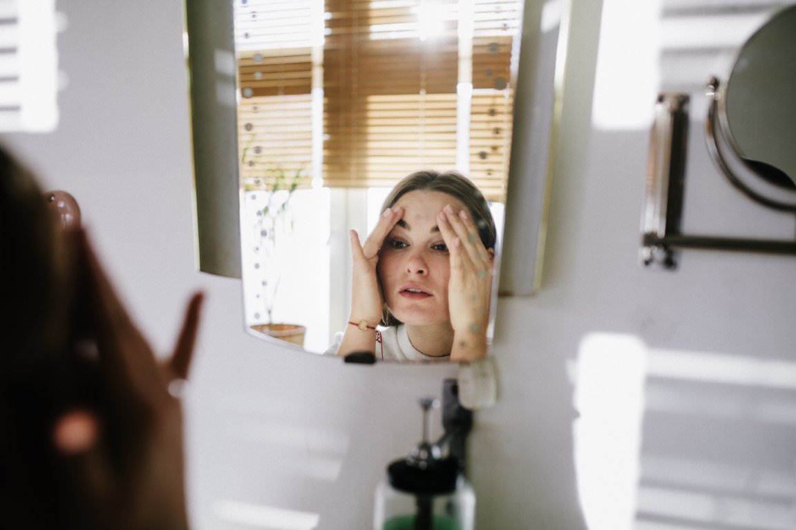 Spiegelbild einer jungen Frau, die sich die über die Stirn streicht