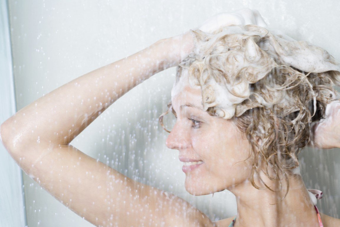 Frau steht unter der Dusche und massiert Shampoo in die Kopfhaut ein