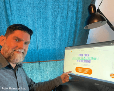 Mann zeigt auf Monitor mit Website zu Neurodermitis-Expertenfinder