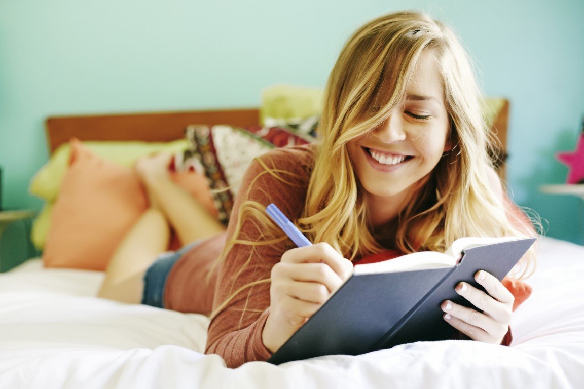 Eine junge Frau schreibt lächelnd in ein Tagebuch