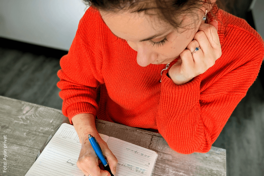 Frau sitzt am Tisch und trägt Termine in einen Kalender ein