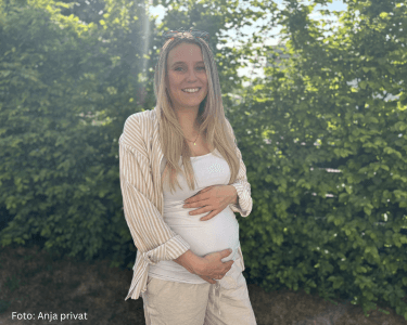 Schwangere Frau steht im Garten und hält ihren Bauch