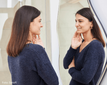 Eine Frau vor einem Spiegel betrachtet ihr Gesicht. Sie hat Erfahrung mit Neurodermitis im Gesicht.