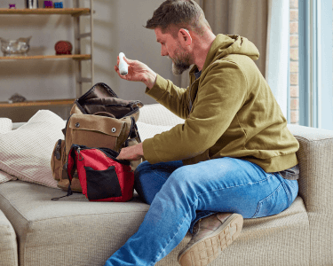 Mann sitzt auf dem Sofa und packt sein Handgepäck für eine Reise mit Neurodermitis und Asthma