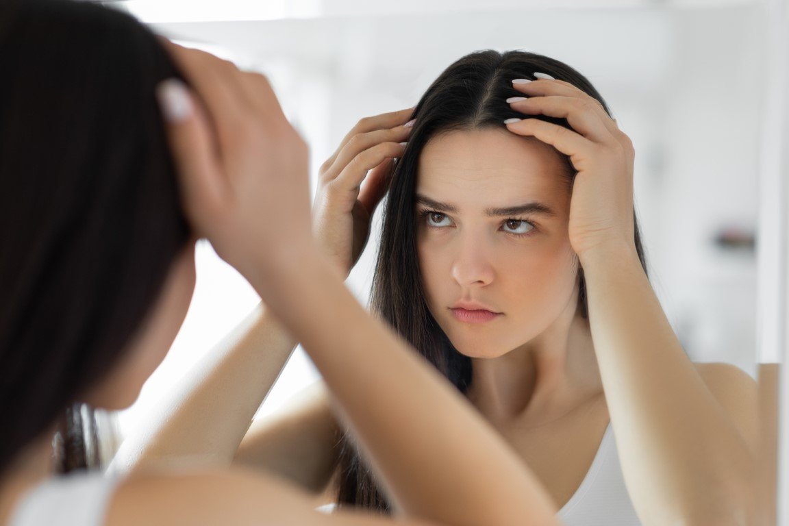 Frau untersucht im Spiegel ihre Kopfhaut