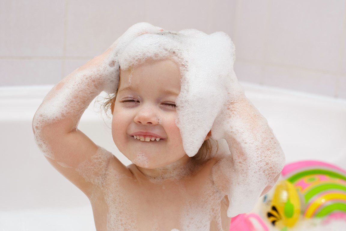 Ein Kleinkind sitzt in der Badewanne und hat Schaum auf dem Kopf