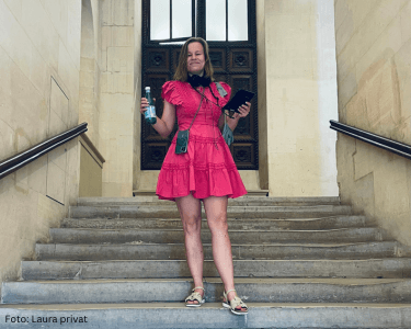Frau im pinken Kleid auf einer Treppe mit Smartphone und Flasche.