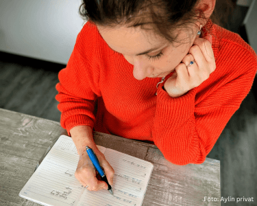 Frau sitzt am Tisch und trägt Termine in einen Kalender ein