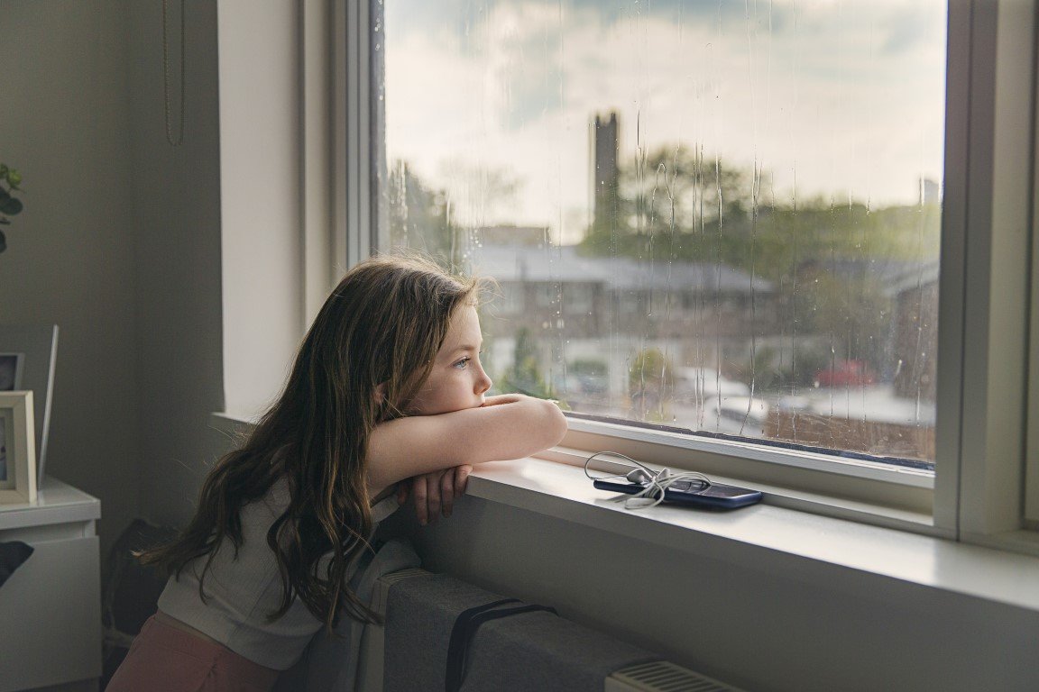 Ein Mädchen blickt traurig aus dem Fenster.