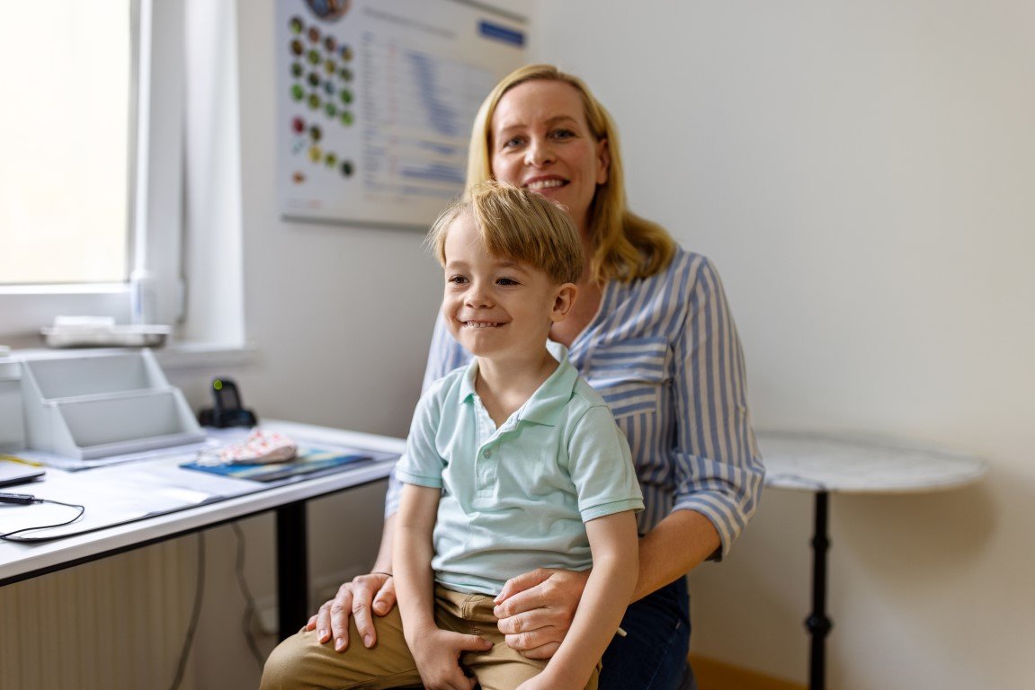 Ein kleiner Junge, der bei einem Arzttermin bei seiner Mutter auf dem Schoß sitzt