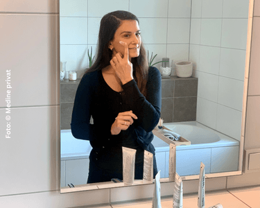 Medine cremt sich ihr Gesicht vor dem Badspiegel ein, um Ihre Neurodermitis zu pflegen