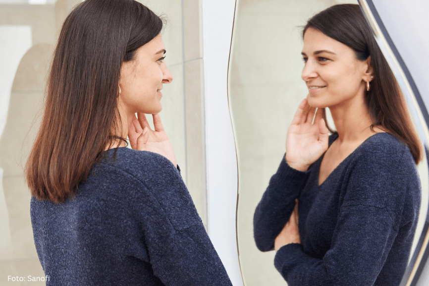 Eine Frau vor einem Spiegel betrachtet ihr Gesicht. Sie hat Erfahrung mit Neurodermitis im Gesicht.