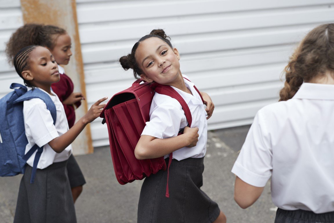 Ein Mädchen trägt einen Schulranzen und lächelt zufrieden.