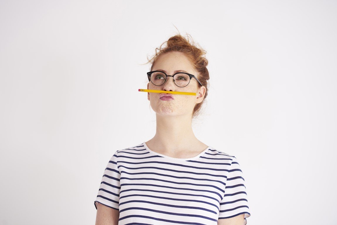 Junge Frau mit Brille, die einen Bleistift zwischen Lippen und Nase klemmt.