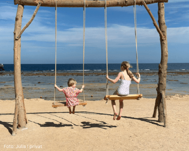 Zwei Kinder auf zwei Schaukeln am Strand – Julia berichtet in ihrem Erfahrungsbericht von ihrem Familienalltag mit Neurodermitis