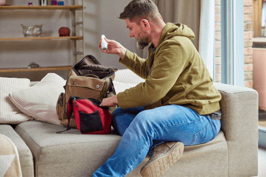Mann sitzt auf dem Sofa und packt sein Handgepäck für eine Reise mit Neurodermitis und Asthma